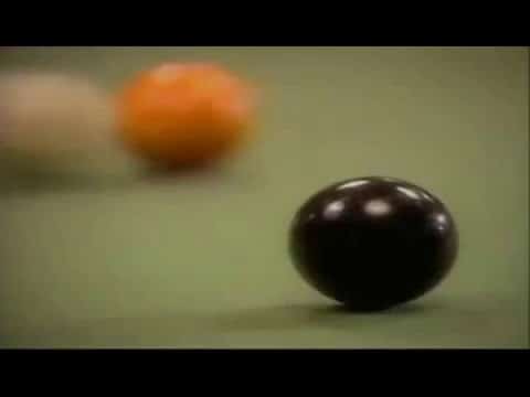 Close-up of a black billiard ball with blurred orange and white balls in the background on a green table.