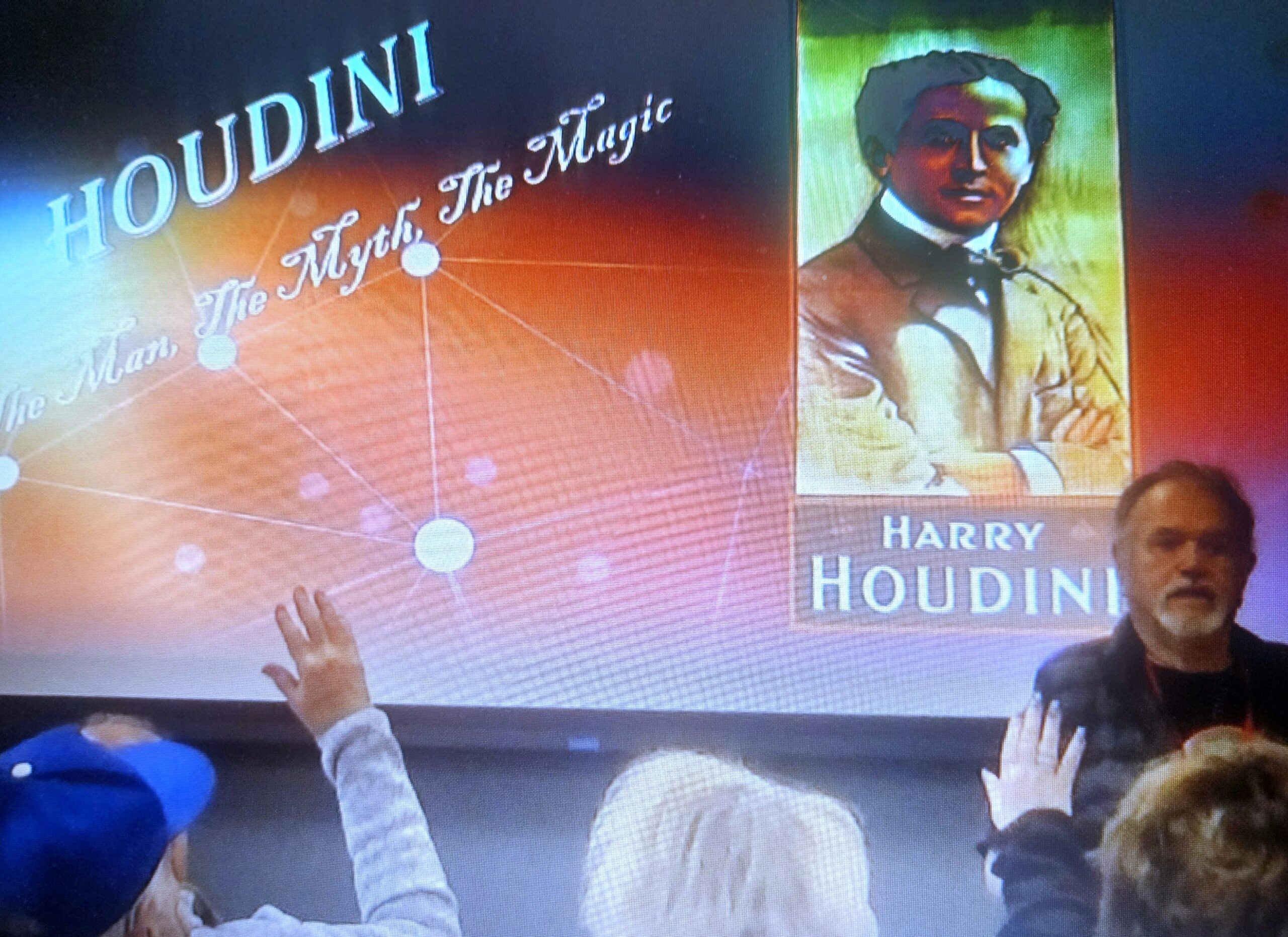 Shell Reinish presents a slideshow titled "Houdini: The Man, The Myth, The Magic" with an illustrated image of Harry Houdini, while audience members raise their hands.