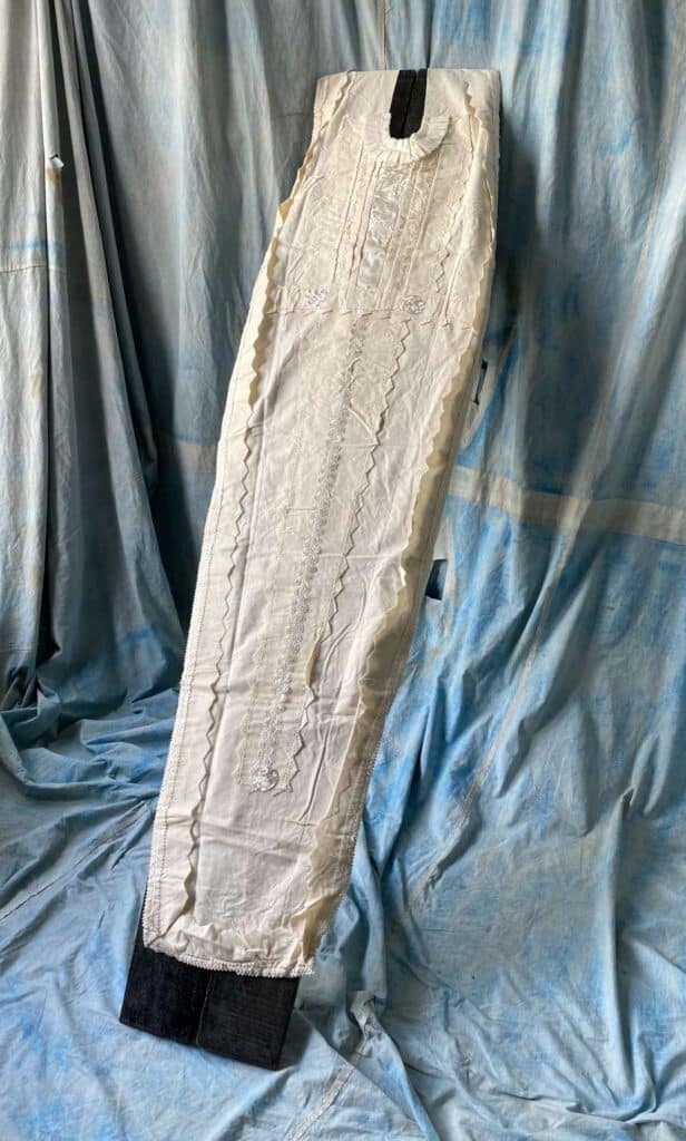 A white padded garment on a hanger, set against a blue draped fabric background.