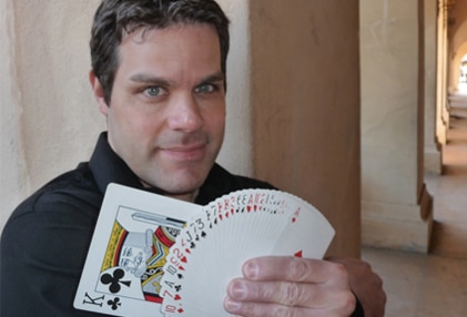 Person holding a fanned-out deck of playing cards, displaying a king of clubs and several red-suited cards, standing in a corridor.